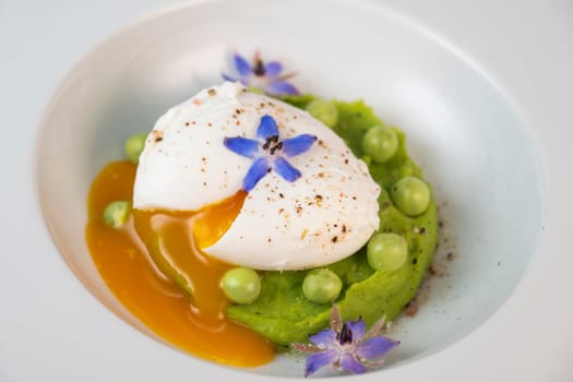 A fresh pea puree is beautifully plated, featuring a poached egg at the center and adorned with borage flowers. The dish showcases vibrant colors and textures, perfect for any spring menu.