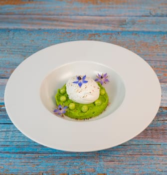 A fresh pea puree is beautifully plated, featuring a poached egg at the center and adorned with borage flowers. The dish showcases vibrant colors and textures, perfect for any spring menu.