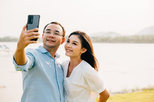 Asian Couple taking selfie picture with smartphone outdoor nature park, Happy smiling woman and man taking photo with mobile phone camera together, Tourist lifestyle people leisure activity