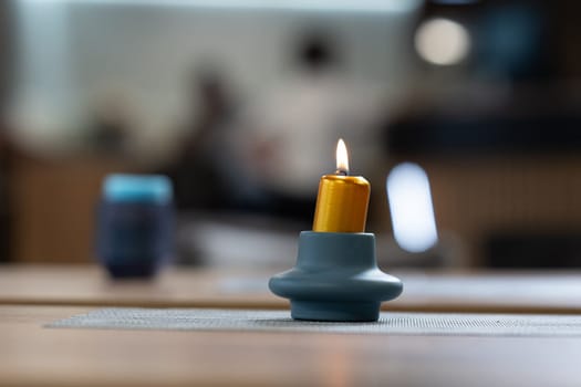 Close-up of a single yellow candle burning on a blue ceramic holder placed on a table.