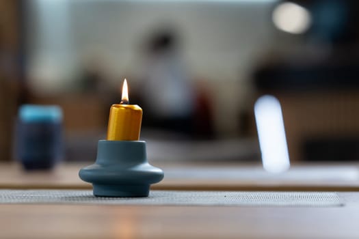 Close-up of a single yellow candle burning on a blue ceramic holder placed on a table.
