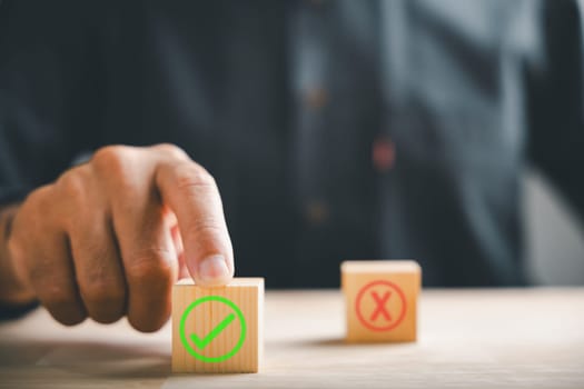 Finger of businessman touches wooden cubes with check marks showing right and wrong choices. Communicates choice validation in decision-making. Think With Yes Or No Choice.