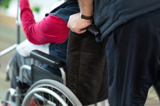 Partial view of a person assisting someone in a wheelchair, showing hands and wheels.
