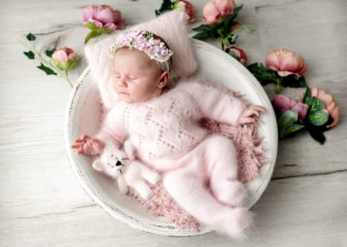 Newborn Baby Girl In Wooden Bowl With Flowers Around During Studio Photoshoot