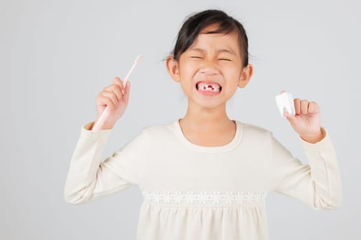 Kid girl holds toothbrush and tooth model, dentist explains tooth loss. Asian child smiles, showing missing milk teeth and gap, promoting dental hygiene habits. isolated white background