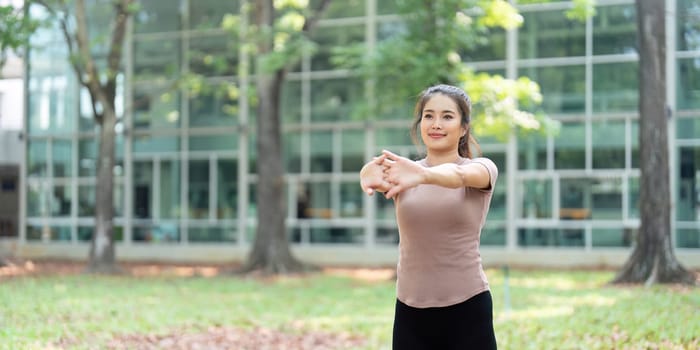 A woman performs arm stretches in a green park, promoting wellness and fitness through outdoor activity.