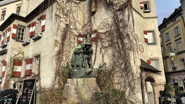 Innsbruck, Austria - March 28, 2025: Old European building with colorful shutters, a traditional architectural style, a bronze statue of two men, known as Monument anon 9 created by Christian Platter 1904 outside, and ivy growing on its walls, located in a picturesque town Innsbruck setting with vibrant atmosphere, highlighting architectural beauty and cultural significance