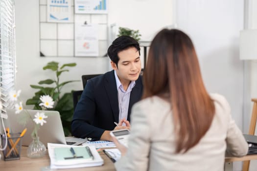 A businessman attentively listening to a female colleague while discussing financial strategies in a bright office environment.