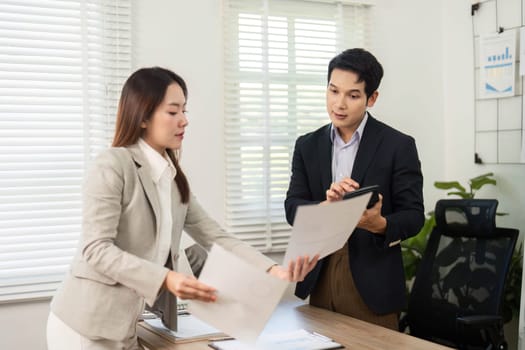 A woman presents documents to a man while discussing project details, highlighting teamwork and professionalism in a corporate setting.