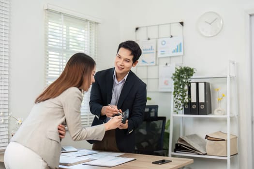 A woman hands over documents to a man while discussing project details, highlighting collaboration and communication in the workplace.