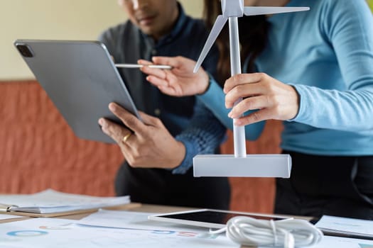 Two colleagues engage in a discussion about renewable energy, using a wind turbine model and digital tools for effective collaboration.