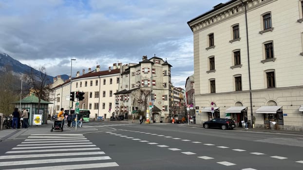 Innsbruck, Austria - March 28, 2025: Historic buildings at urban busy street in Innsbruck with people, historic architecture, pedestrians crossing and vehicles, display architectural charm, vibrant urban life and a scenic street view with cars, bus