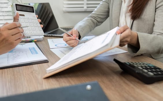 Two professionals engage in a financial strategy discussion, reviewing documents and utilizing a calculator for accurate analysis.