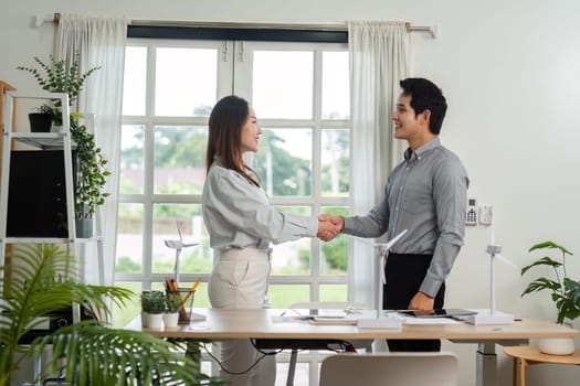 Two business professionals shake hands, celebrating their successful collaboration on an ESG initiative in a bright office.