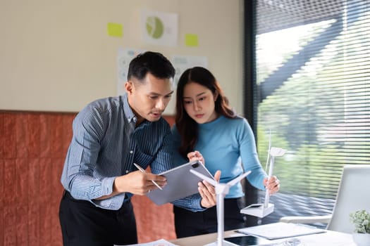 A team discusses renewable energy solutions, analyzing a wind turbine model and digital data on tablets in a modern workspace.