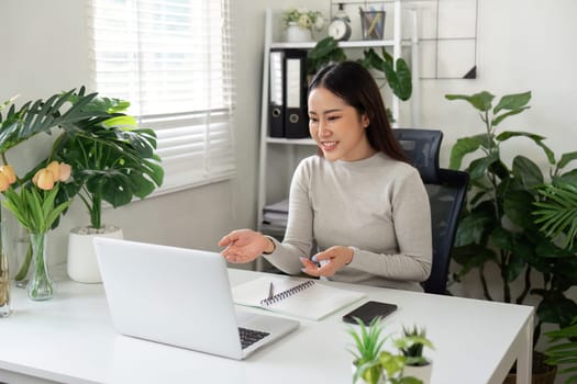 A woman engaging in a video call, sharing ideas and smiling in a bright home office filled with plants.