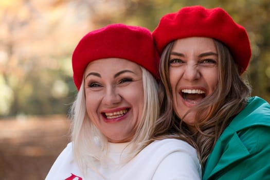 Two women, wearing matching red berets, laugh joyfully together outdoors in an autumnal setting. Close-up portrait showcasing their happiness.