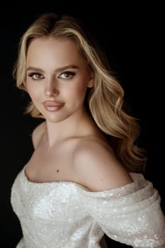 Young, fair-haired woman with wavy hair. Beautiful model with long hair. Blonde with perfect make-up and styling. In a white dress with open shoulders.