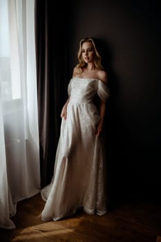 Elegant bridal gown showcased in a minimalist setting with a model in a chic pose during an indoor shoot. A graceful bride poses in a long, white wedding dress. High quality photo