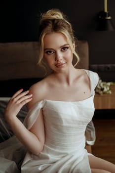 Beautiful bride Fashion portrait in wedding luxury dress with lace and crystals in dark interior. Blonde happy woman wears wedding white dress with wedding makeup and hairstyle. Newlywed.