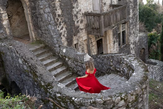 Woman in a red dress stands on a stone staircase within the ruins of a decaying castle. The dress billows slightly.