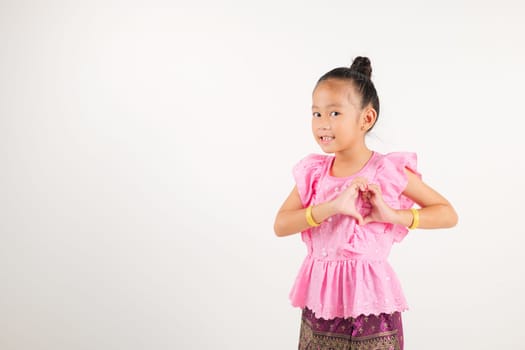 Portrait Thailand kid girl smiling traditional Thai dress costume shows creating heart shape with fingers and hands, studio isolated white background, kindergarten child sending love for Valentine day