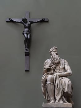 London, UK - May 07, 2025 - Marble statue of Moses by Michelangelo with The striking figure of Jesus Christ crucified on the Cross in the green wall background. The Moses is a sculpture by the Italian Renaissance artist Michelangelo Buonarroti, Displayed in The V&A (Victoria and Albert Museum) in London, use it as your Wallpaper, Poster and Space for text, Selective focus.