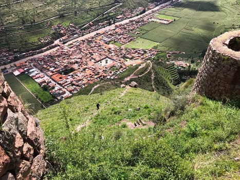 Tourist descending a steep hillside with inca ruins and the town of pisac in the sacred valley, cusco, peru