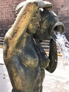 Bronze fountain statue of a woman pouring water from a clay pot in cusco, peru