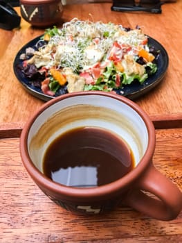 Freshly brewed coffee served in a traditional peruvian clay mug alongside a healthy salad in a cusco restaurant