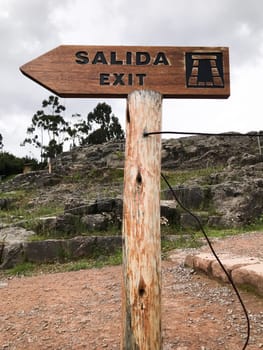 Wooden exit sign with salida and exit written on it, pointing the way out of inca ruins in cusco, peru