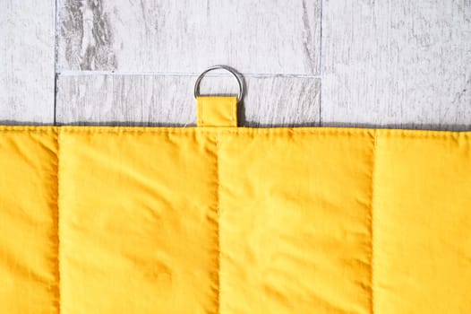 Yellow quilted pet blanket with metal ring hanging on light wooden wall, creating cozy and welcoming space for pets