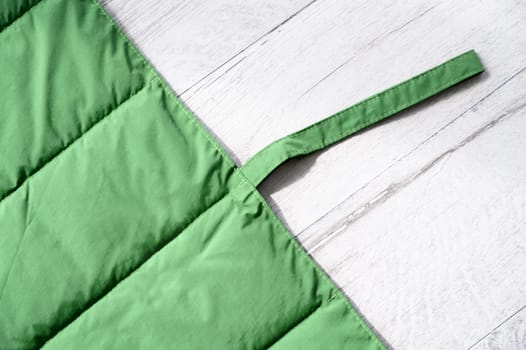 Close up of a green padded and quilted pet friendly mat with carrying handle, perfect for travel, resting on a white wooden floor