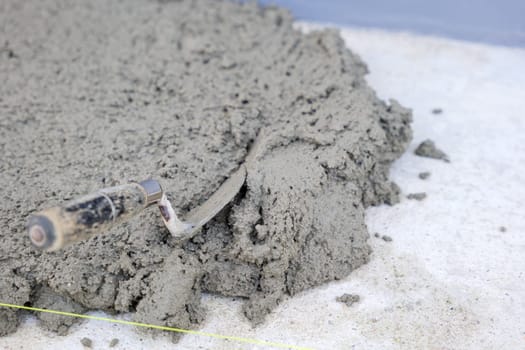 Close-up view of tiling tools: a trowel, pull tabs, and wedges lying on gray concrete, emphasizing the meticulous process of tile installation and leveling.