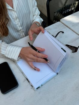 Writing ideas in a journal while seated at a cafe table, with a phone beside and sunglasses nearby.