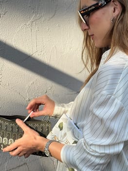 A woman dressed in a striped top is focused on a stylus as she interacts with a device, holding a stylish clutch in her other hand.