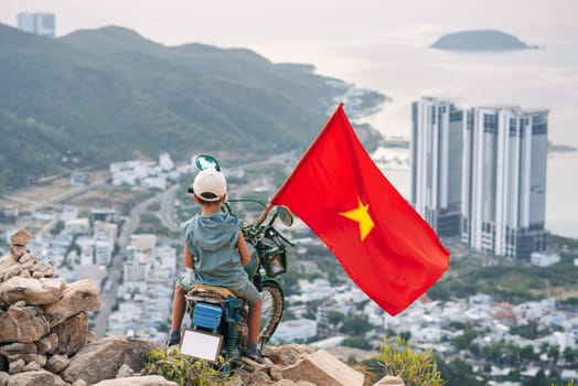 Back of tourist child boy on motorcycle on top of a mountain with a Vietnam flag. Mountain of Angels in Nha Trang in Vietnam