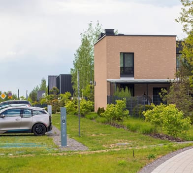Facade of the stylish, urban, modern house, ergonomically designed and made of ecological materials. Electrical vehicle charging station next to it.