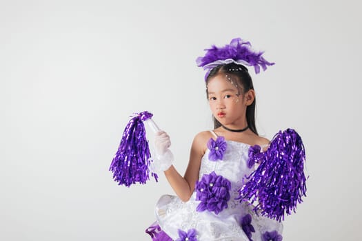 Smiling cheerleader girl wearing purple and white outfit with pom-poms. Studio portrait exuding energy and joy against a white background. cheerleader kid
