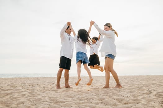 Beachside jubilation as an Asian family with father and mother holding children jumps into air. beautiful ocean serves as stunning backdrop highlighting family's happiness and playful bond.