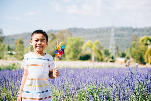 Little boy's portrait amid a flower garden joyfully holding a toy pinwheel. Springtime happiness and flying pinwheel signify fun in nature's sunny embrace evoking childhood joy.