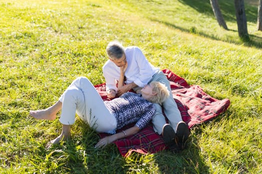 Romantic senior couple enjoying a relaxing summer picnic in a park, lying on a blanket on the grass
