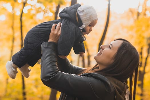 Autumn scene of mother holding young baby girl outdoors with colorful trees in park