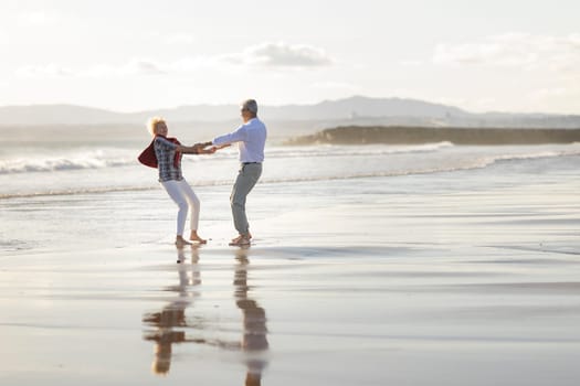 Elderly couple holding hands and spinning around on a wet sandy beach at sunset