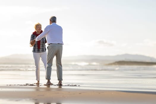 Elderly couple enjoying a romantic moment, dancing barefoot on the beach during a beautiful sunset