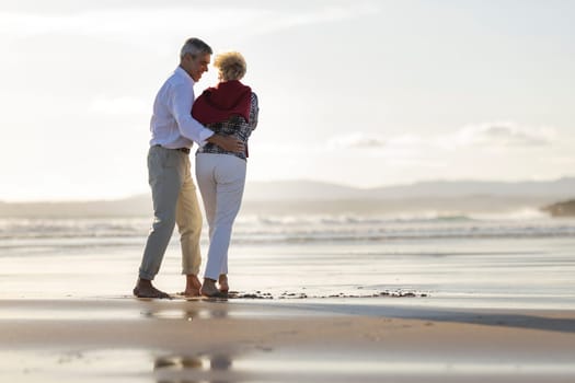 Happy retired couple embracing and walking on the beach at sunset, enjoying peaceful retirement