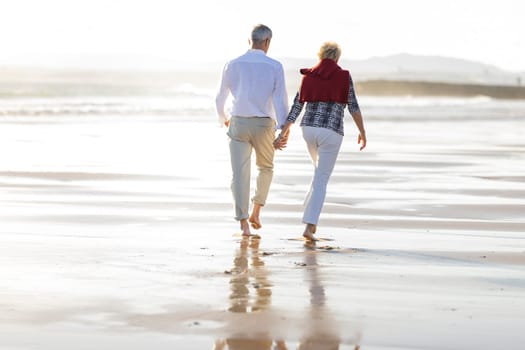 Retired couple enjoying walking on the beach at sunset, holding hands