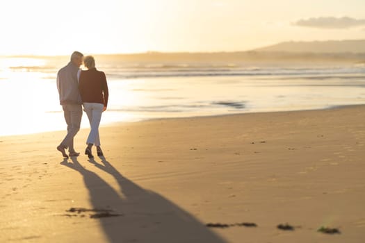 Senior couple walking on beach at sunset, enjoying golden hour light