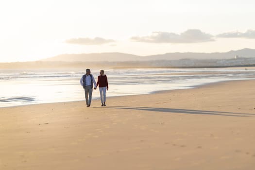 Elderly couple enjoying a romantic walk on the beach at sunset