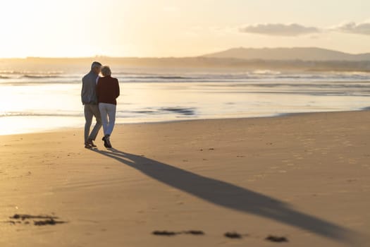 Elderly couple enjoying a romantic walk on the beach during a golden sunset, celebrating their retirement